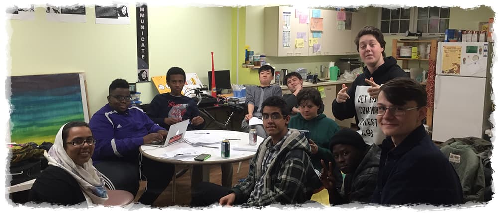 Groupe de jeunes rassemblés dans une salle communautaire, participant à une activité collaborative et souriant à l'appareil photo.